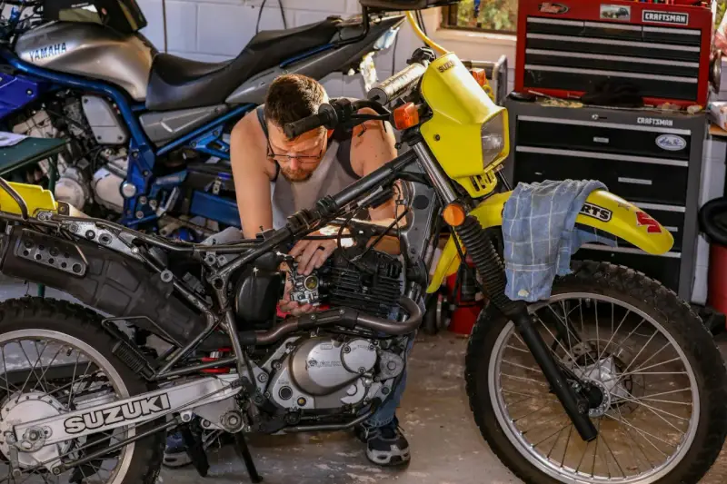 Mężczyzna majstruje przy żółtym motocyklu Suzuki. Rozrusznik kręci, a motocykl nie odpala.