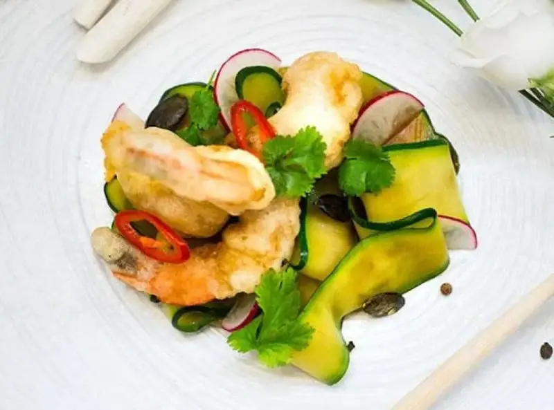 Chrupiące tempura do krewetek z cukinią, rzodkiewką i chili na białym talerzu.