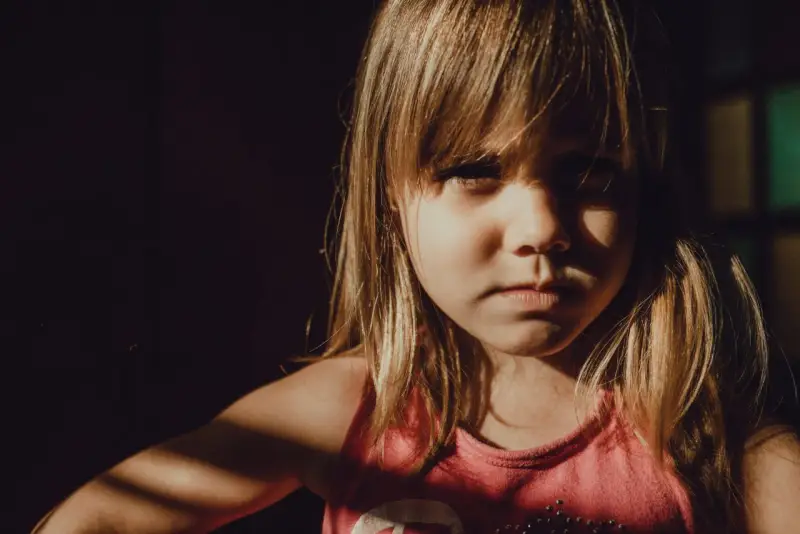 Niña con expresión seria, con luz de ventana en su rostro. A veces, mi hijo de 9 años se enoja por todo, pero hoy solo mira con intensidad.