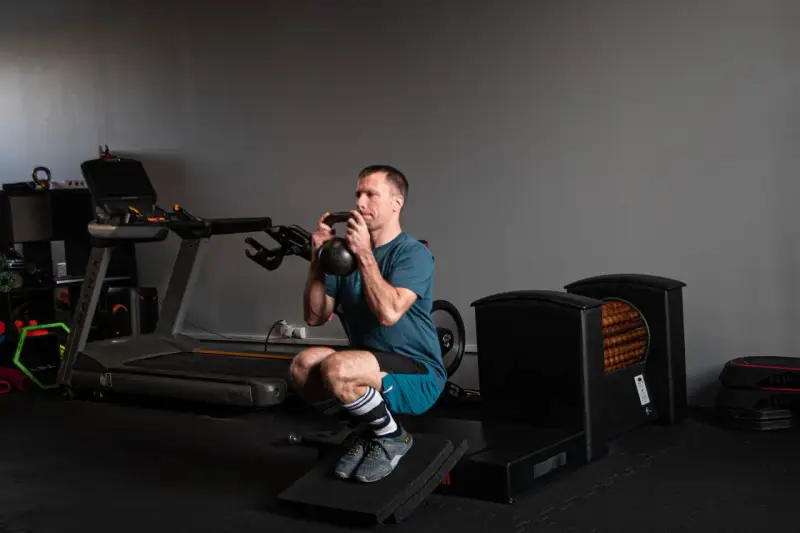 Mężczyzna wykonuje głęboki **squat** z kettlebell w rękach, ćwicząc siłę w siłowni.
