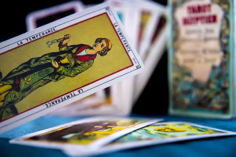 Rozłożone karty tarot 3 karty: "La Tempérance" w centrum, inne karty w tle i pudełko z napisem "Tarot".
