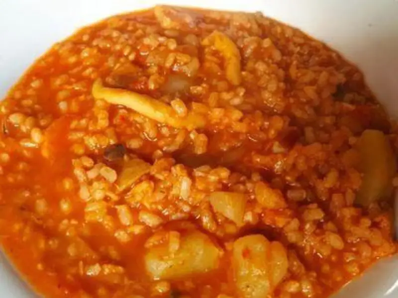 Arroz caldoso con trozos de marisco y verduras en salsa rojiza.