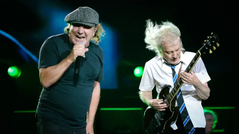 Brian Johnson śpiewa, Angus Young gra na gitarze podczas jednego z legendarnych **AC/DC koncertów**.