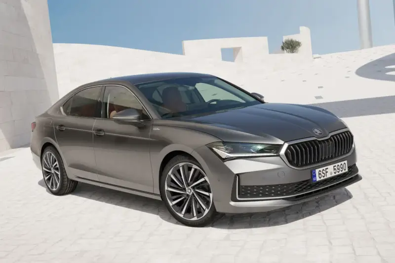 Szary sedan Skoda Superb, segment d, zaparkowany na tle nowoczesnej architektury.