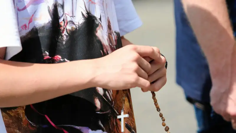 Dłoń trzyma paciorki różańca, a na koszulce widnieje biały krzyż. To znak modlitwy, żeby się wszystko ułożyło.