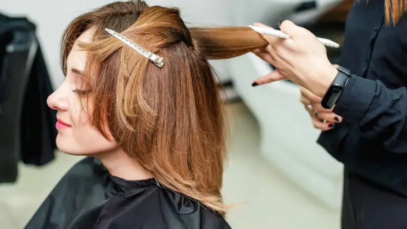 Fryzjerka modeluje włosy do ramion cieniowane, tworząc subtelne przejścia.