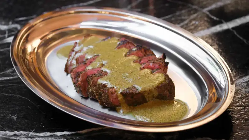 Tranché de bœuf, nappé d'une sauce verte, une spécialité parisienne servie sur un plateau métallique.
