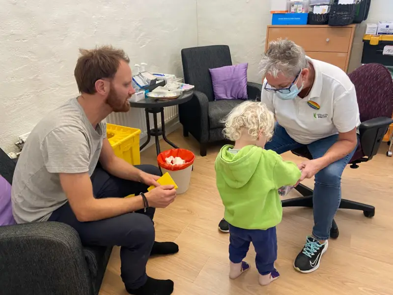 En pappa och ett barn får vaccin av en sjuksköterska. Barnet verkar lite oroligt, men sjuksköterskan är lugn och trygg. Det är en fin stund av vaccin italien.
