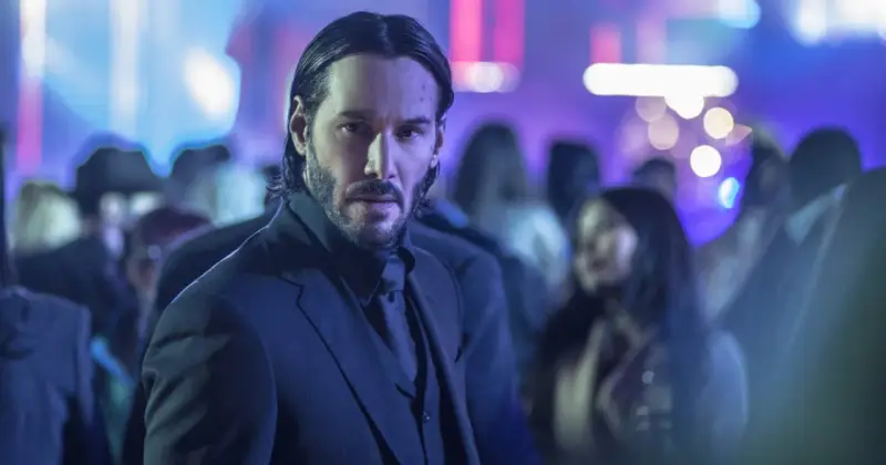 Keanu Reeves w garniturze, w tle rozmyte światła i tłum. Ikona kina akcji, znana z filmów takich jak John Wick.