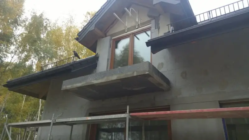 Budowa domu w toku, trwa ocieplenie ścian. Widać rusztowania i niedokończony balkon.