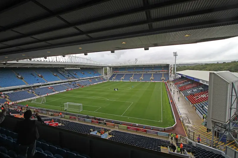 Widok na murawę i trybuny stadionu Ewood Park. Puste miejsca na niebieskich i czerwonych siedzeniach.