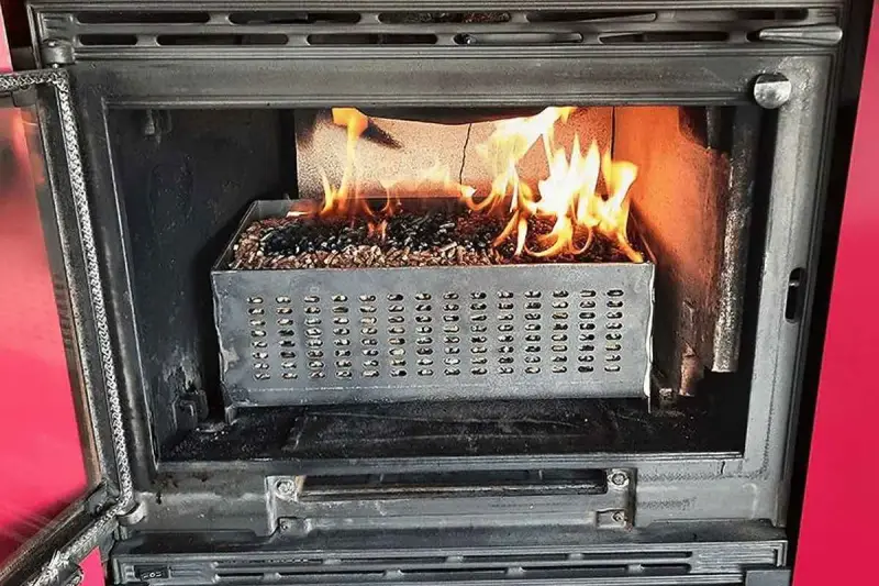 Estufa de pellets ardiendo dentro de un hueco de chimenea. El combustible se quema en una bandeja metálica perforada.