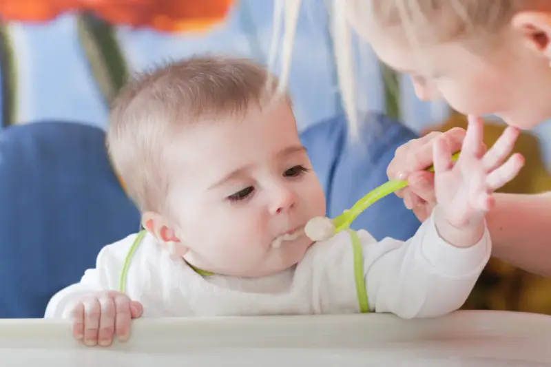 Mama karmi dziecko łyżeczką do karmienia niemowląt. Maluch z zaciekawieniem patrzy na jedzenie.
