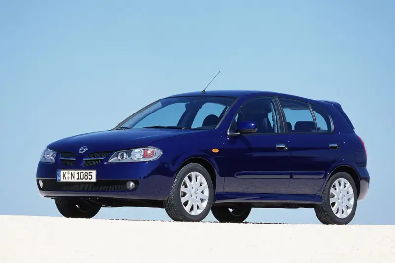 Granatowy Nissan Almera stoi na białym tle, z błękitnym niebem w tle.