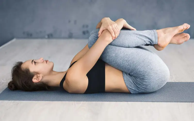 Frau in Yoga-Pose, Knie zur Brust gezogen. Ein Geheimtipp bei Ischias zur Linderung von Rückenschmerzen.