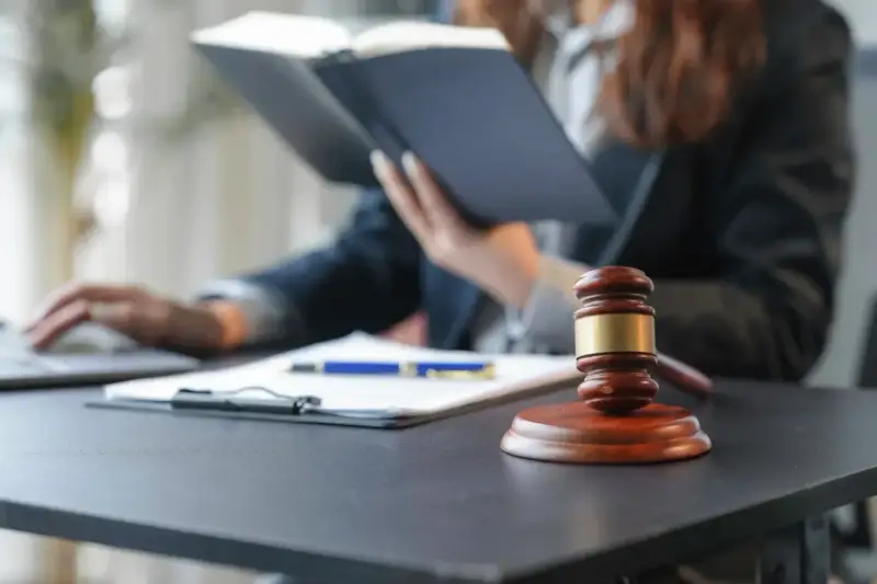 Sądowy młotek i dokumenty na biurku. Prawnik w tle studiuje akta, zastanawiając się, czy radca prawny może być obrońcą.