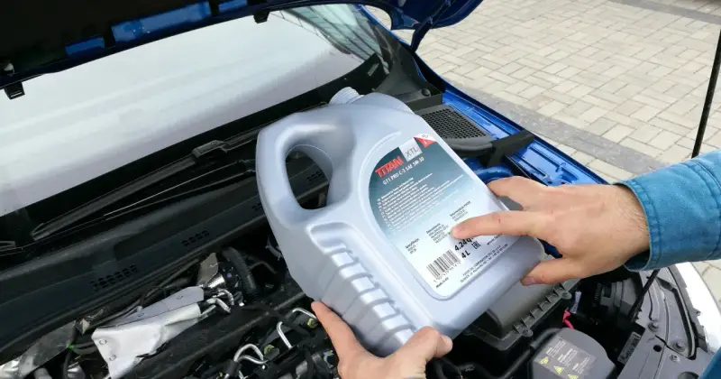 Osoba trzymająca kanister oleju silnikowego TITAN GT1 PRO C-3 SAE 5W-30 nad silnikiem. Czy można mieszać oleje silnikowe? Sprawdź specyfikacje!