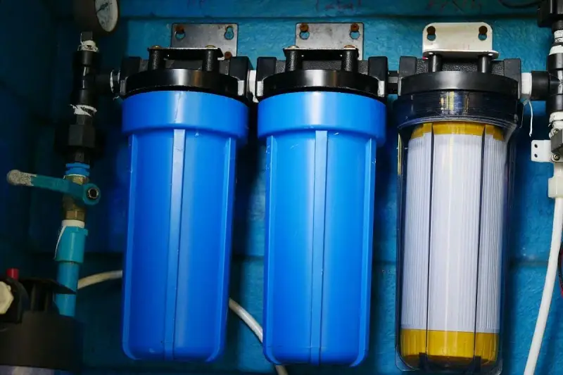 System filtrów do wody, który oczyszcza wodę. Dwa niebieskie filtry i jeden przezroczysty z białym wkładem.