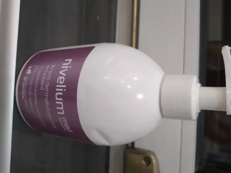 Biała butelka z pompką, na której widnieje napis "nivelium med krem dermatologiczny emolient". Idealny dla skóry z AZS i łuszczycą.