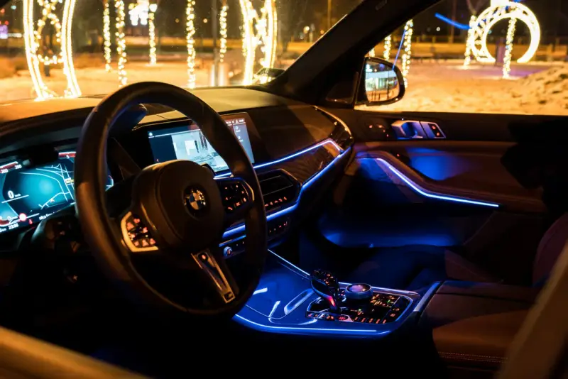Wnętrze luksusowego BMW x5 nocą, oświetlone niebieskim ambientowym światłem. Za oknem świąteczne iluminacje.