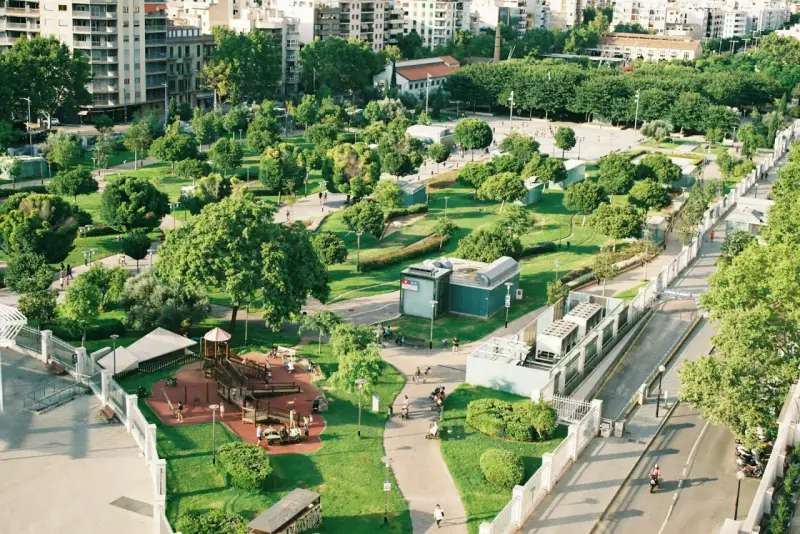 Park z placem zabaw i alejkami, otoczony budynkami. Wygląda jak jeden z najbardziej zielonych miast w Polsce.