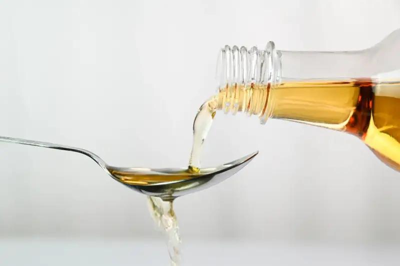 Apfelessig wird aus einer Flasche auf einen Löffel gegossen. Ein Tropfen für das Abnehmen.