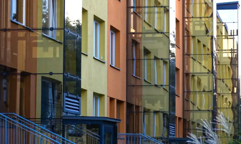 Nowoczesny blok z żółtymi i pomarańczowymi elewacjami, przeszklonymi klatkami schodowymi. Czy ustawa o windach wymusi montaż dźwigów w niskich blokach z czwartego piętra?