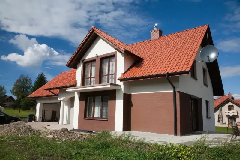 Jaki kolor elewacji do czerwonego dachu? Biała elewacja z brązowymi akcentami, jak na tym domu, wygląda stylowo.