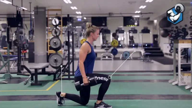 Kvinna utför utfallssteg med vikt i ett gym. Hon håller en hantel i ena handen och har ett ben framåt och ett bakåt.
