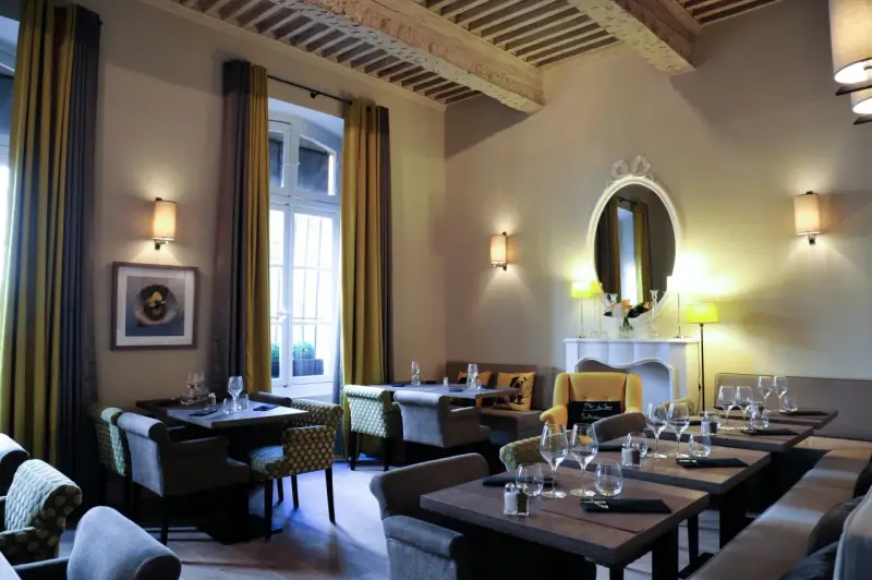 Salle à manger élégante avec tables dressées, fauteuils confortables et un miroir orné. L'ambiance évoque une **spécialité provençale** raffinée.