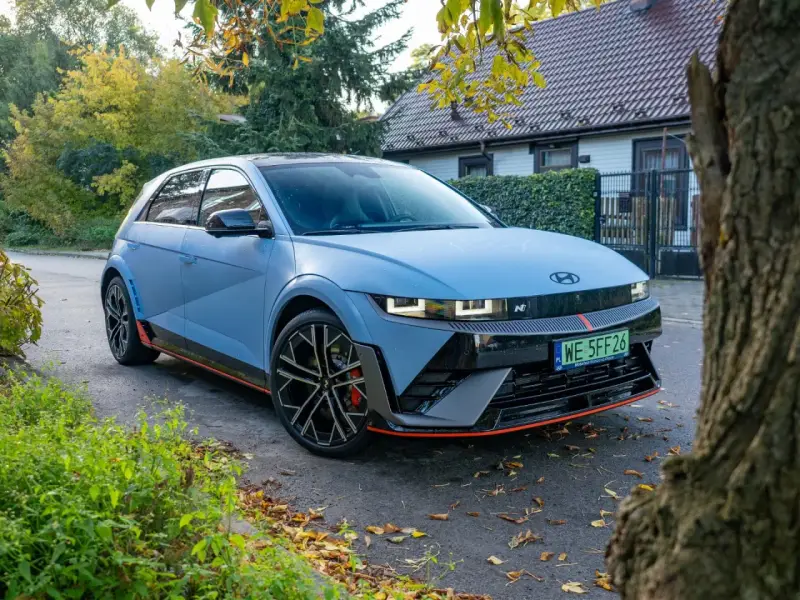 Niebieski Hyundai Ioniq 5 N z czerwonymi akcentami stoi na tle domu i drzew.