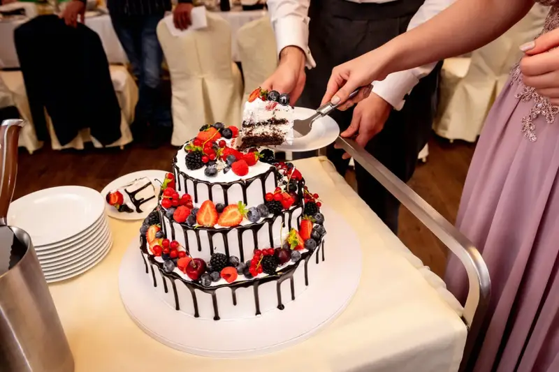 Piękne torty weselne z owocami, ozdobione czekoladą i świeżymi jagodami, malinami i truskawkami. Para kroi pierwszy kawałek.