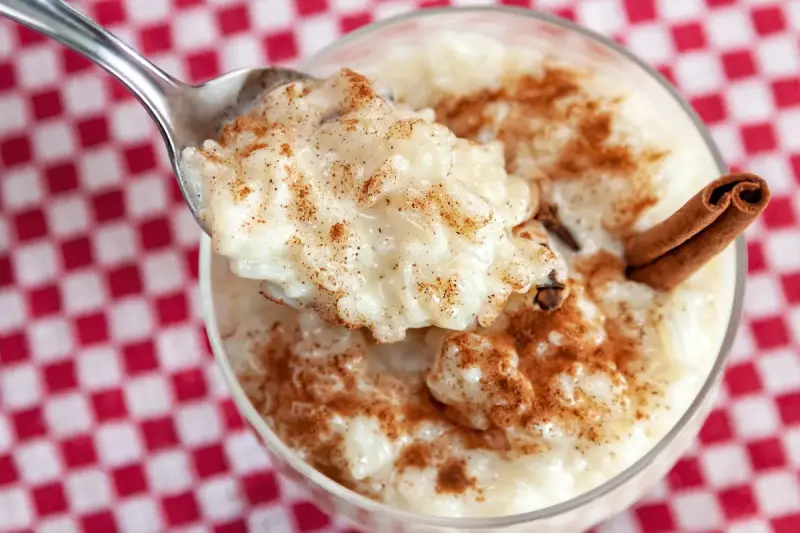 Cuchara con cremoso arroz con leche, espolvoreado con canela. ¿Quién inventó el arroz con leche? ¡Este postre es un clásico!