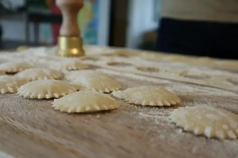 Świeże ravioli na drewnianej desce, posypane mąką. Zastanawiasz się, ravioli z czym podawać?