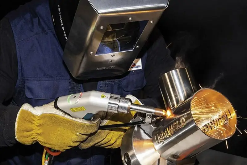 Operator w masce spawalniczej wykonuje napawanie laserowe metalowych elementów, tworząc iskrzące spoiny.