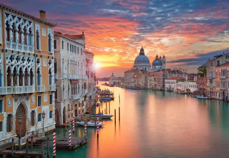 Tramonto sul Canal Grande, un quadro perfetto di posti romantici a Venezia. Palazzi storici e la Basilica di Santa Maria della Salute riflettono i colori del cielo.