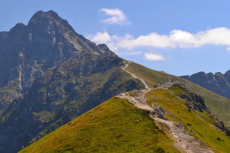 Kamienista ścieżka wije się po zielonych zboczach, prowadząc turystów ku majestatycznym tatry zachodnie szczyty.