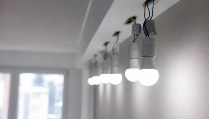 Rząd białych żarówek LED, wiszących na przewodach, świeci jasno, mimo że instalacja wygląda na nieukończoną.