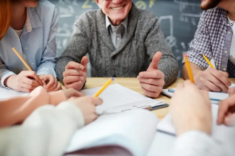 Uśmiechnięty nauczyciel w stanie nieczynnym, otoczony przez studentów piszących notatki.