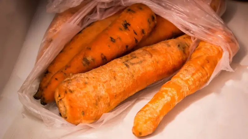 Kilka pomarańczowych marchewek w plastikowej torbie, na których widać ciemne plamy, oznaki pleśni.