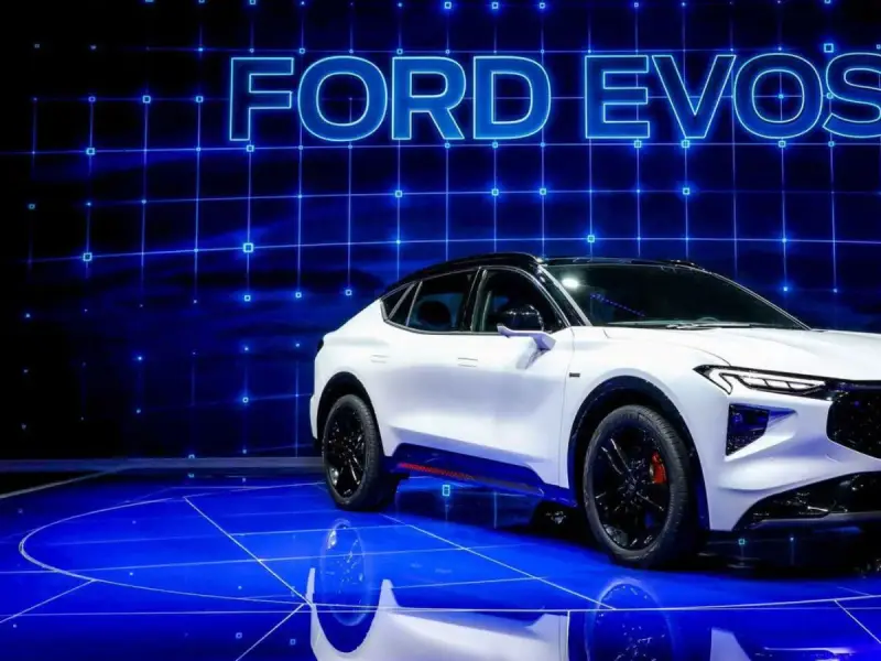 Biały Ford Evos na niebieskim, futurystycznym tle z siatką. Elegancka linia nadwozia i sportowe detale podkreślają jego nowoczesny charakter.