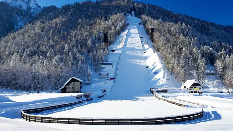 Zimowa Planica w Alpach Julijskich, z ośnieżoną skocznią narciarską i lasem iglastym.