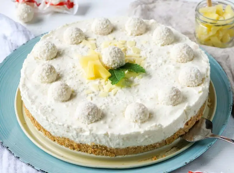 Eine köstliche Raffaello Torte ohne Backen, dekoriert mit Kokosbällchen, Ananas und Minze.