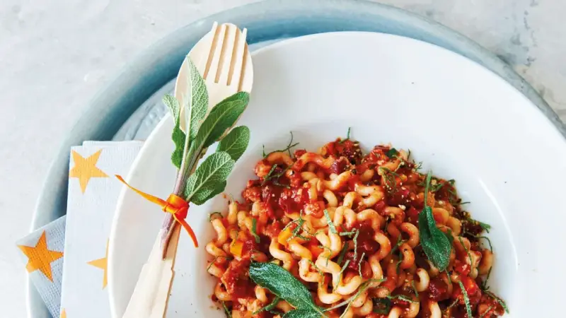Gedrehte Pasta mit Bolognese-Sauce, garniert mit Salbei. Ein Holzgabel-Set mit Kräutern, passend zur bolognese schwangerschaft.
