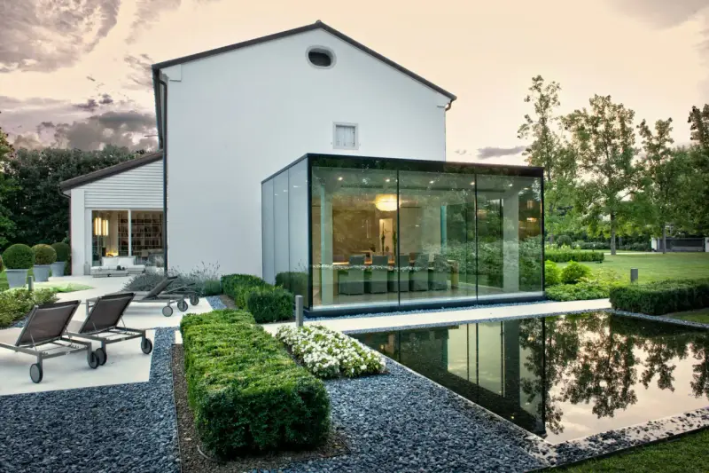 Ampliamento casa con estensione esterna in vetro, con piscina e arredi da giardino.