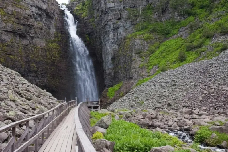 Vacker vattenfall i en ravin, med en träbro som leder besökare längs en av Sveriges många vandringsleder.