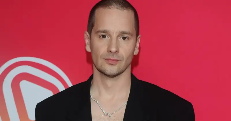 Krzysztof Zalewski w czarnym garniturze, z naszyjnikiem, na tle czerwonym z białym logo.
