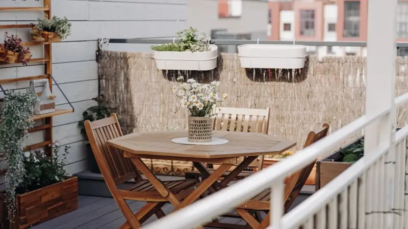 Holztisch mit Stühlen und Gänseblümchen, Wandregal mit Pflanzen, schöne Balkon Ideen für Ihr Zuhause.