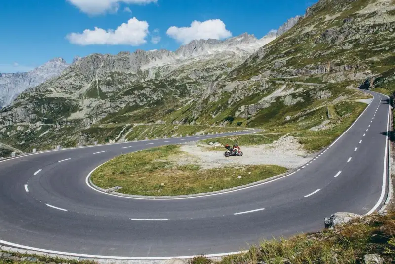 Una moto attende su un tornante del Grimsel Pass, tra montagne verdi e cielo azzurro.