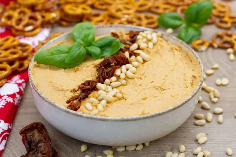 Aksamitny hummus z suszonymi pomidorami i orzeszkami pinii, udekorowany listkami bazylii. Idealny do chrupiących precelków.